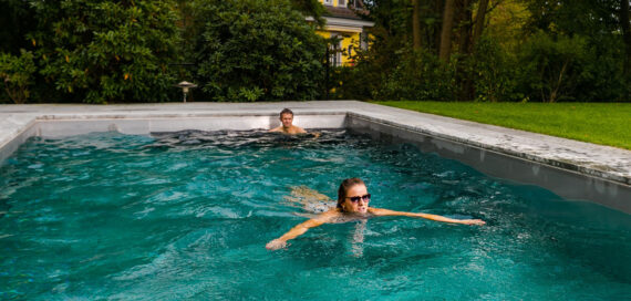 In einem privatem Garten schwimmen ein Mann und eine Frau mit Sonnenbrille in einem Pool von FlussPool