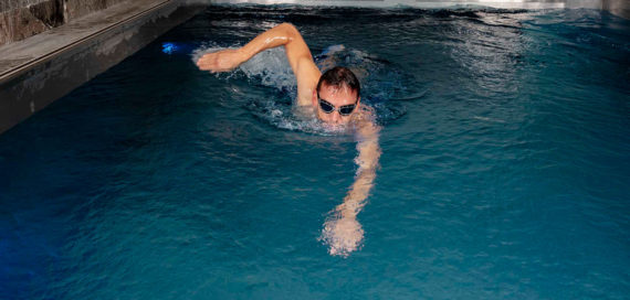 Ein Mann schwimmt in einem Gegenstrompool aus Edelstahl von FlussPool. Er hat eine Schwimmbrille an und ist frontal von vorne zu sehen.